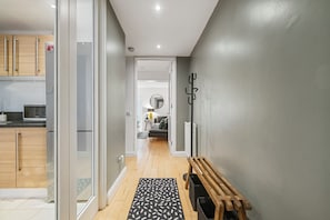 A hallway with a wooden bench, a black trash bin, and a patterned rug. - Exclusive & Comfortable Home by Old Street Station (London)