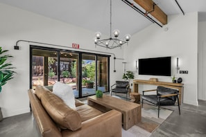 A modern interior with a sofa, chairs, a wooden table, a TV, and a large window with an exit sign. - Adults Only Zion Escape: New Vacation Rental #3 (Springdale)