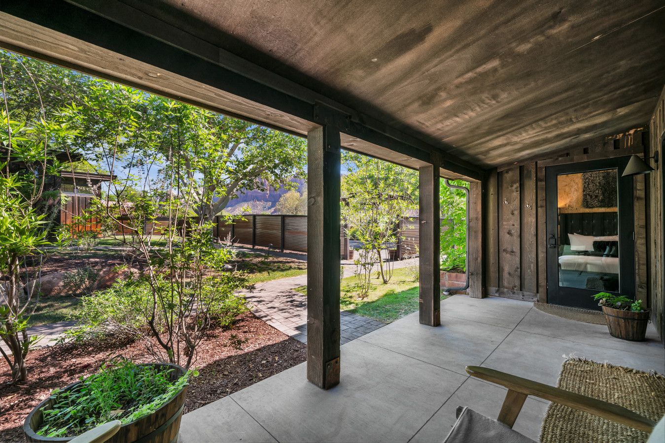 Un espace extérieur abrité, doté d’un sol en béton, de piliers en bois et offrant une vue sur un quartier résidentiel avec des arbres et une maison.