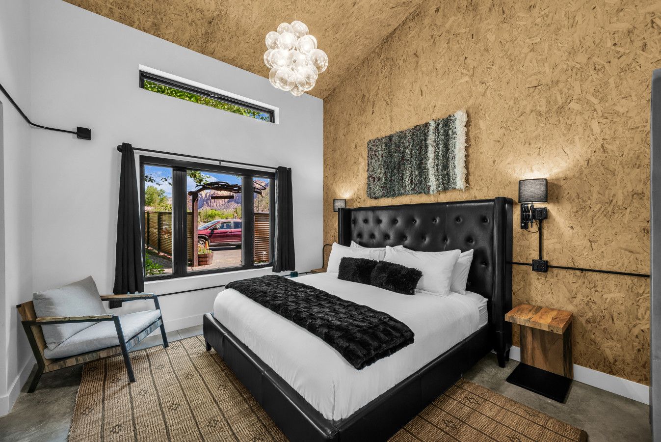 A bedroom with a large bed, a window with a view, a wooden wall, and a modern light fixture.