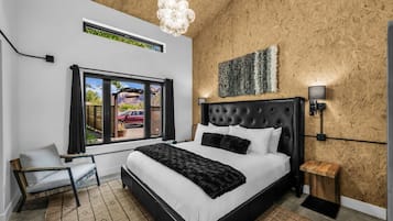 A bedroom with a large bed, a window with a view, a wooden wall, and a modern light fixture.