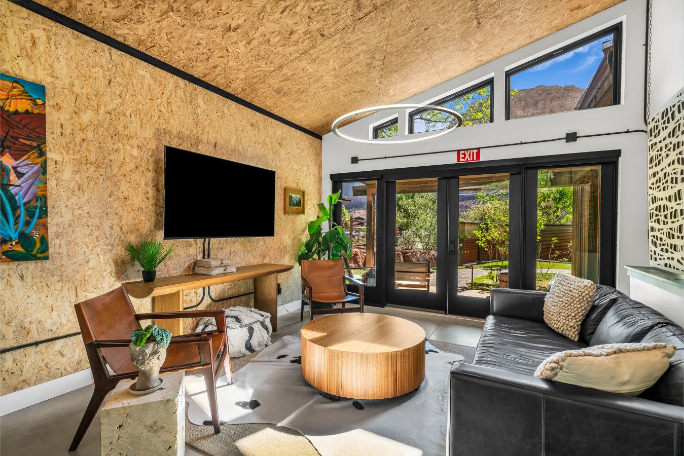 Ein modernes Interieur mit Holzboden, einem Flachbildfernseher, einem Essbereich und einer Couch mit Blick ins Freie.