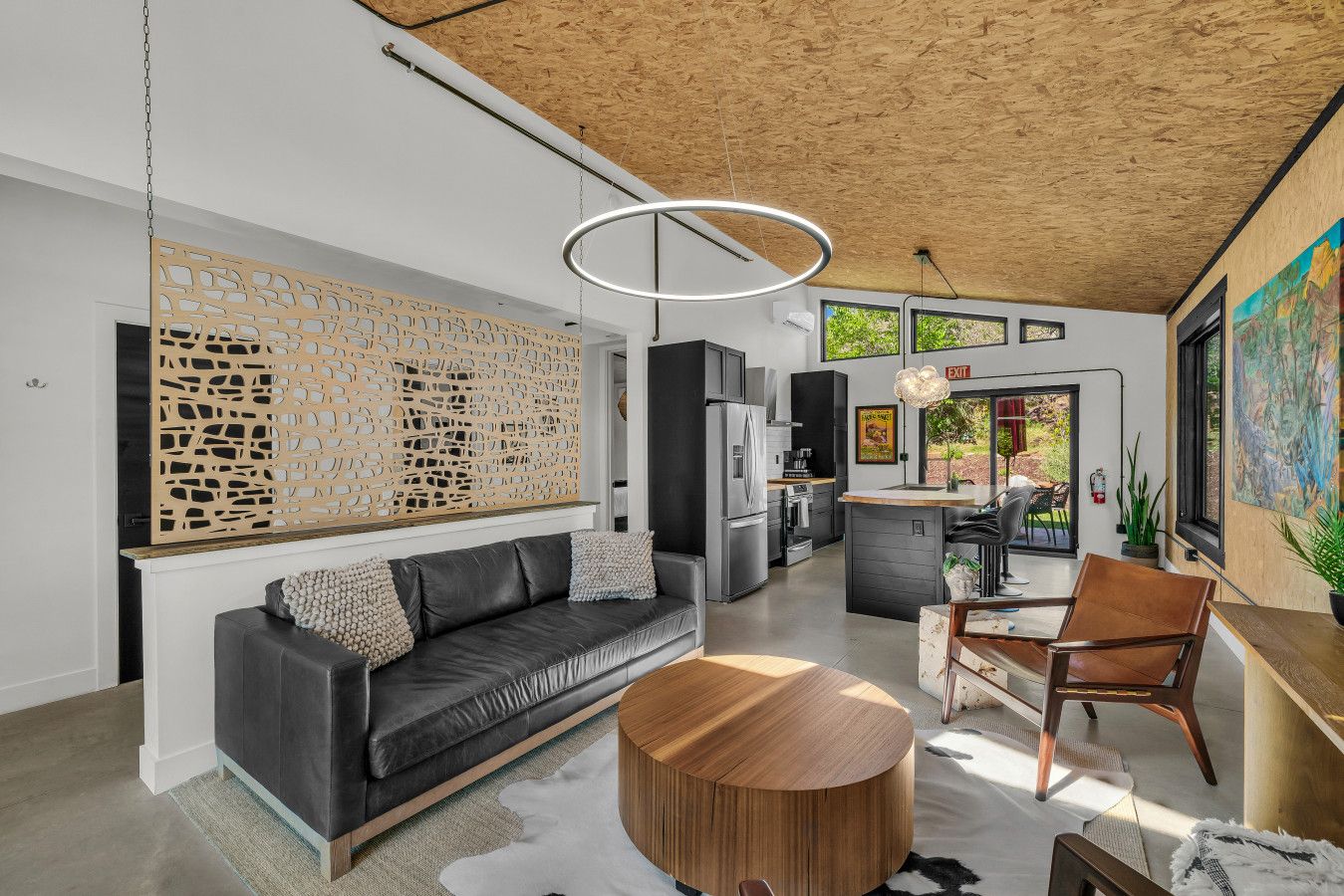 A modern living room with a black leather sofa, a wooden coffee table, and a dining area with a wooden table and chairs.