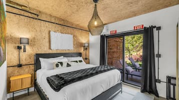 Ein Schlafzimmer mit einem Bett, einem Nachttisch, einer Lampe, einem Fluchtwegschild und Blick ins Freie.