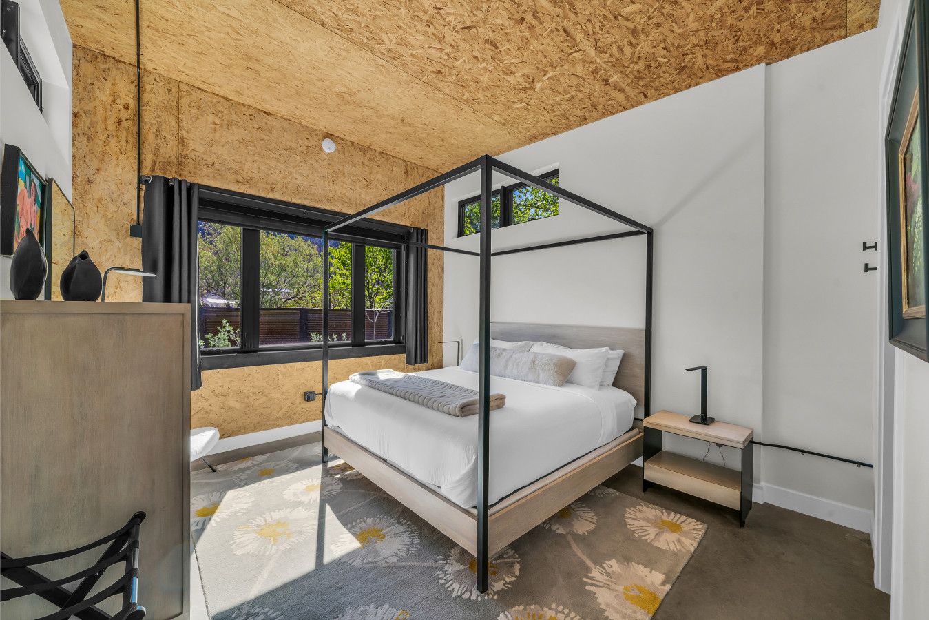 A bedroom with a four-poster bed, a desk, and a window with a view of trees.