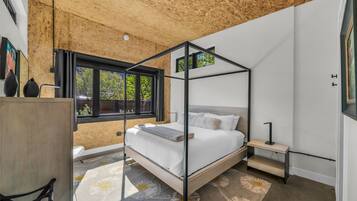 A bedroom with a four-poster bed, a desk, and a window with a view of trees.