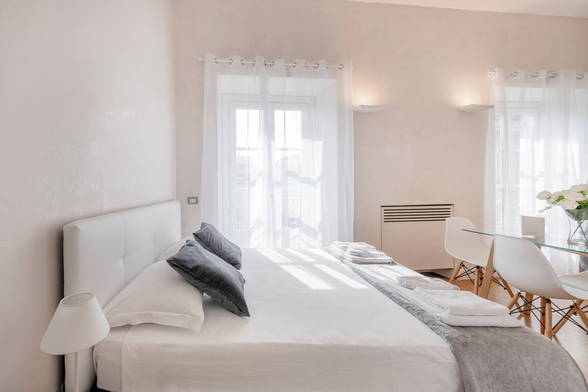 A modern hotel room with a neatly made bed, a glass table, and a chair.