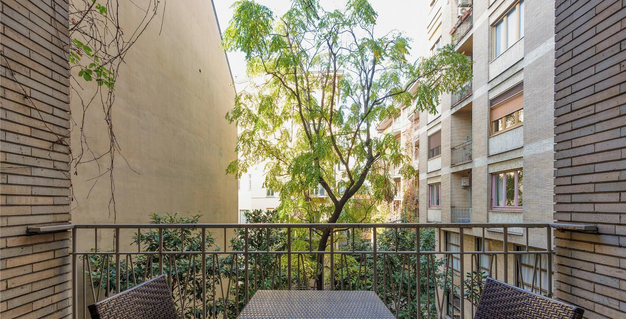 A balcony with wicker furniture, a view of a tree, and a building with multiple windows and balconies.