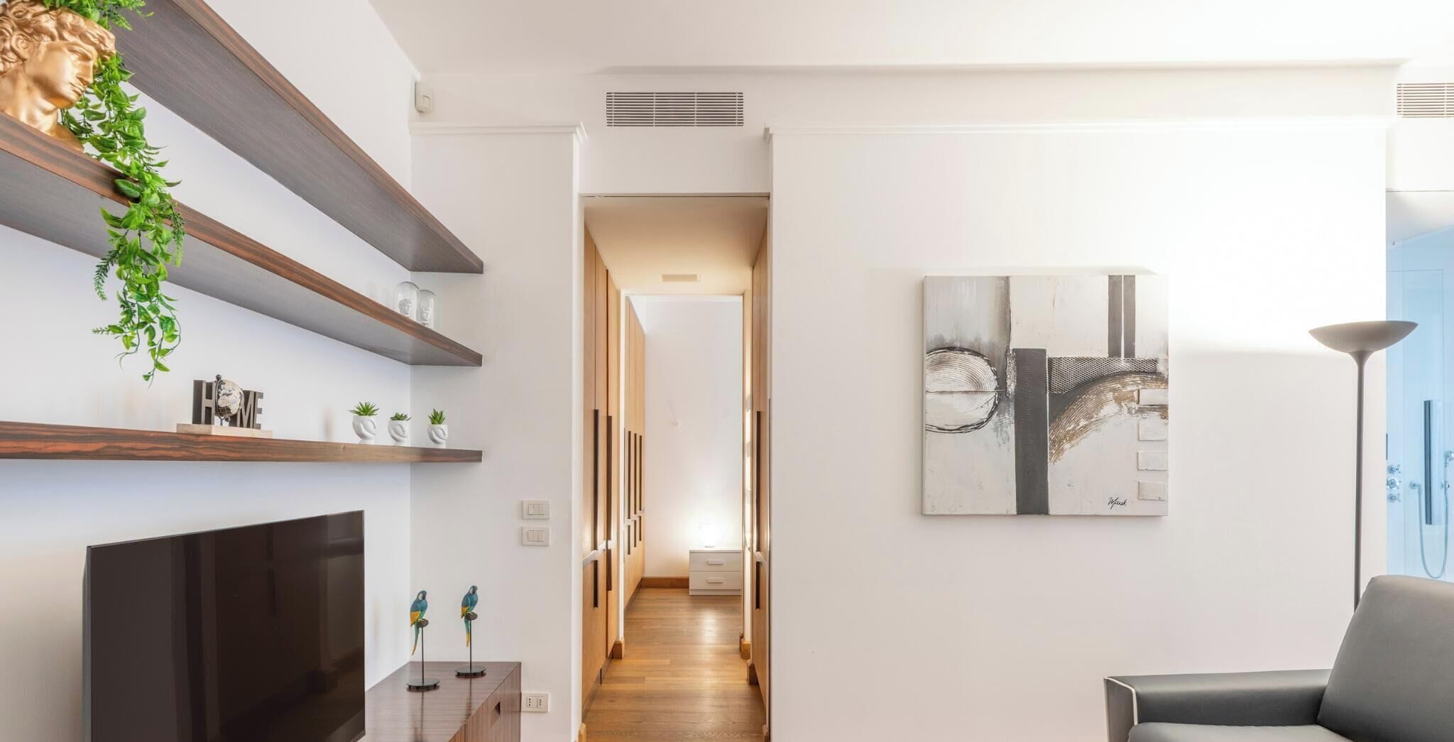 A modern living room with a flat-screen TV, wooden shelves, and a painting.