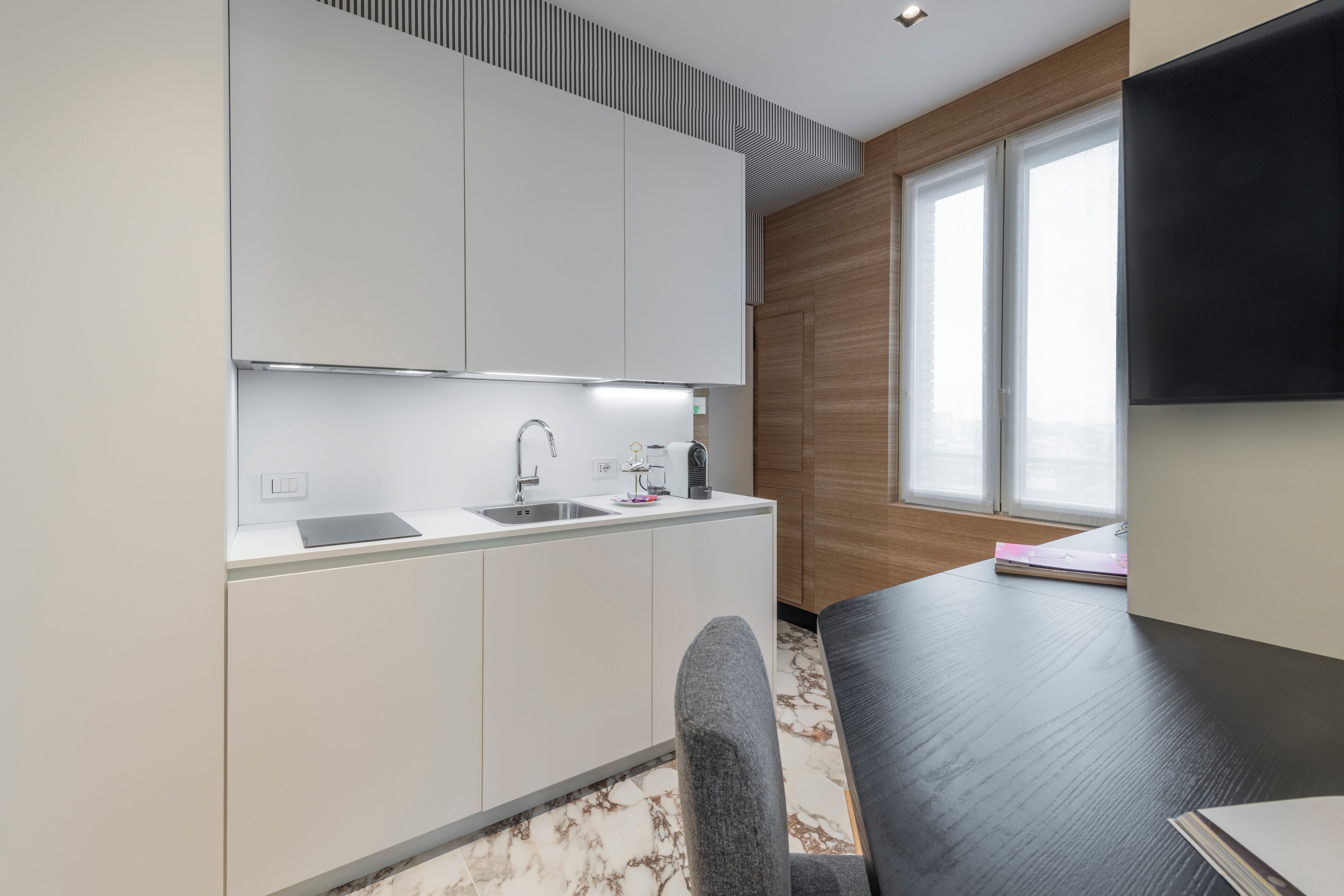 A modern kitchen with white cabinets, a black countertop, and a marble backsplash.
