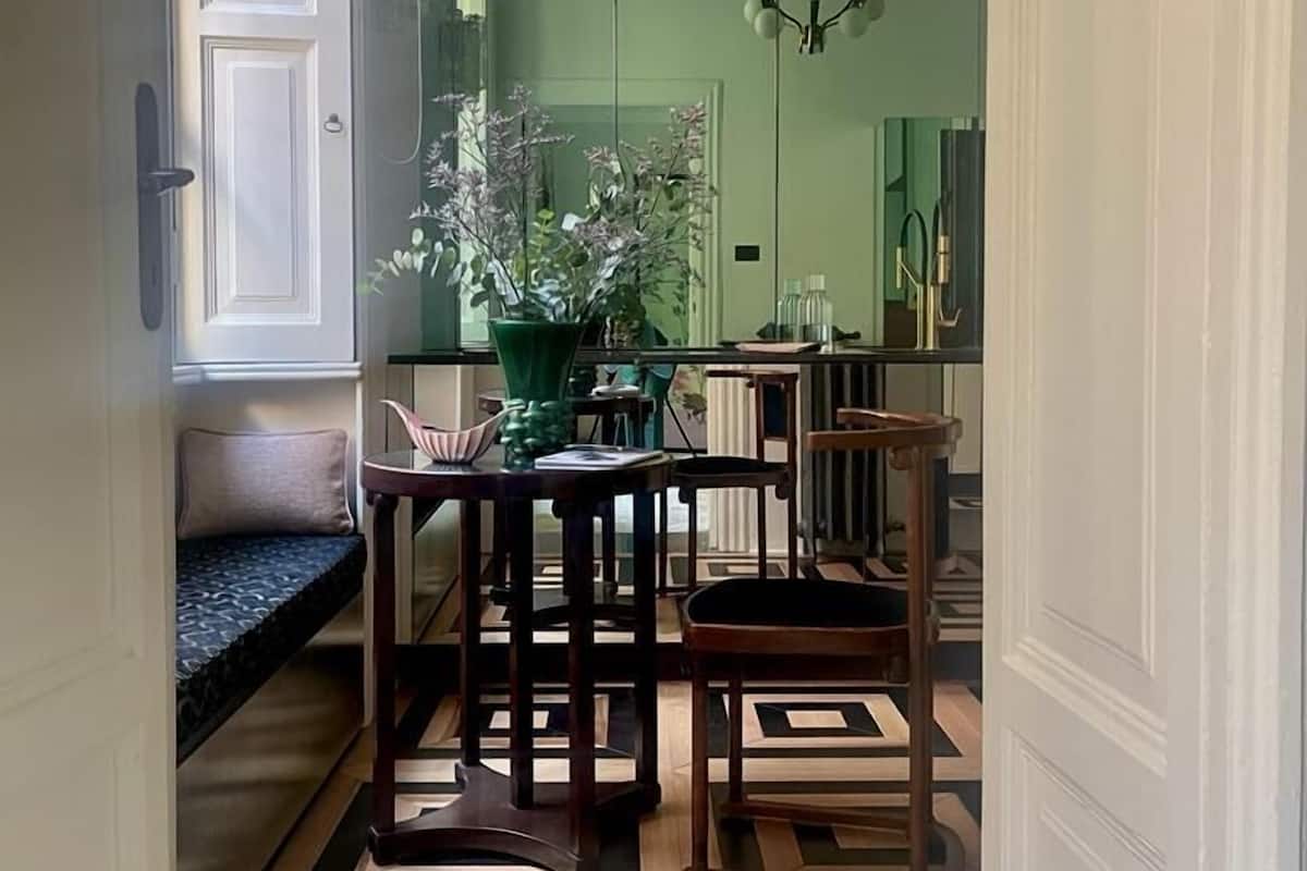 A narrow hallway with a wooden bench, a dining table with chairs, a potted plant, and a geometric patterned floor.