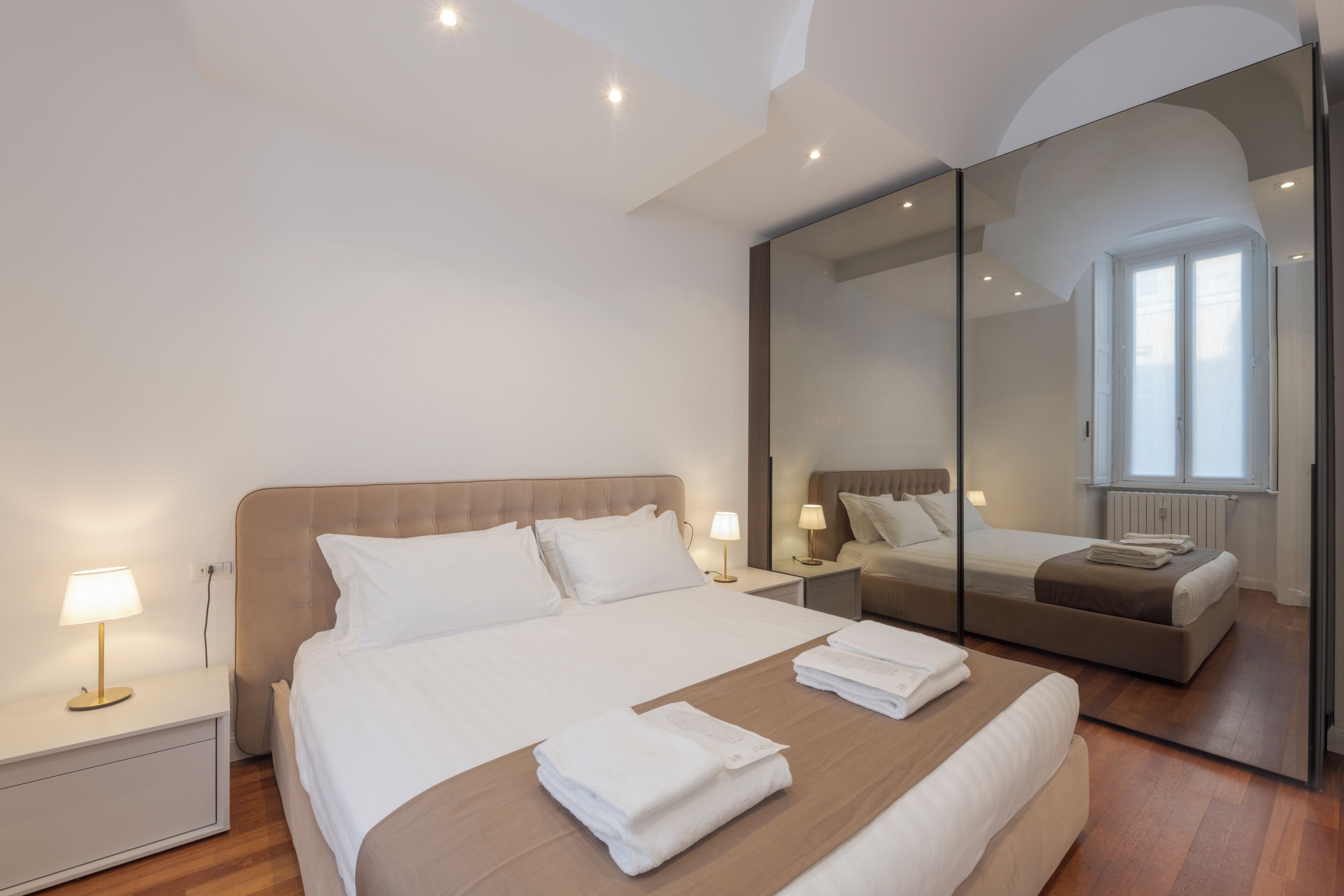 Un dormitorio moderno con una cama grande, mesitas de noche, un espejo y una ventana.