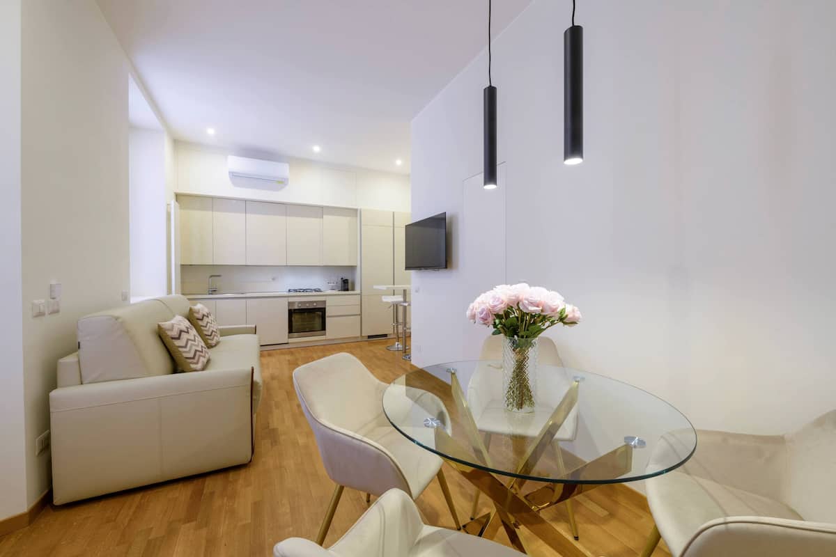 A modern living space with a glass dining table, white sofas, and a kitchen in the background.