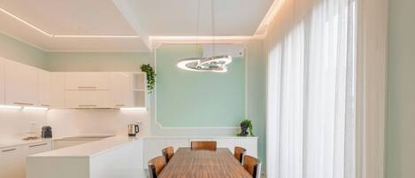 A modern kitchen with white cabinets, a wooden dining table, and pendant lighting.