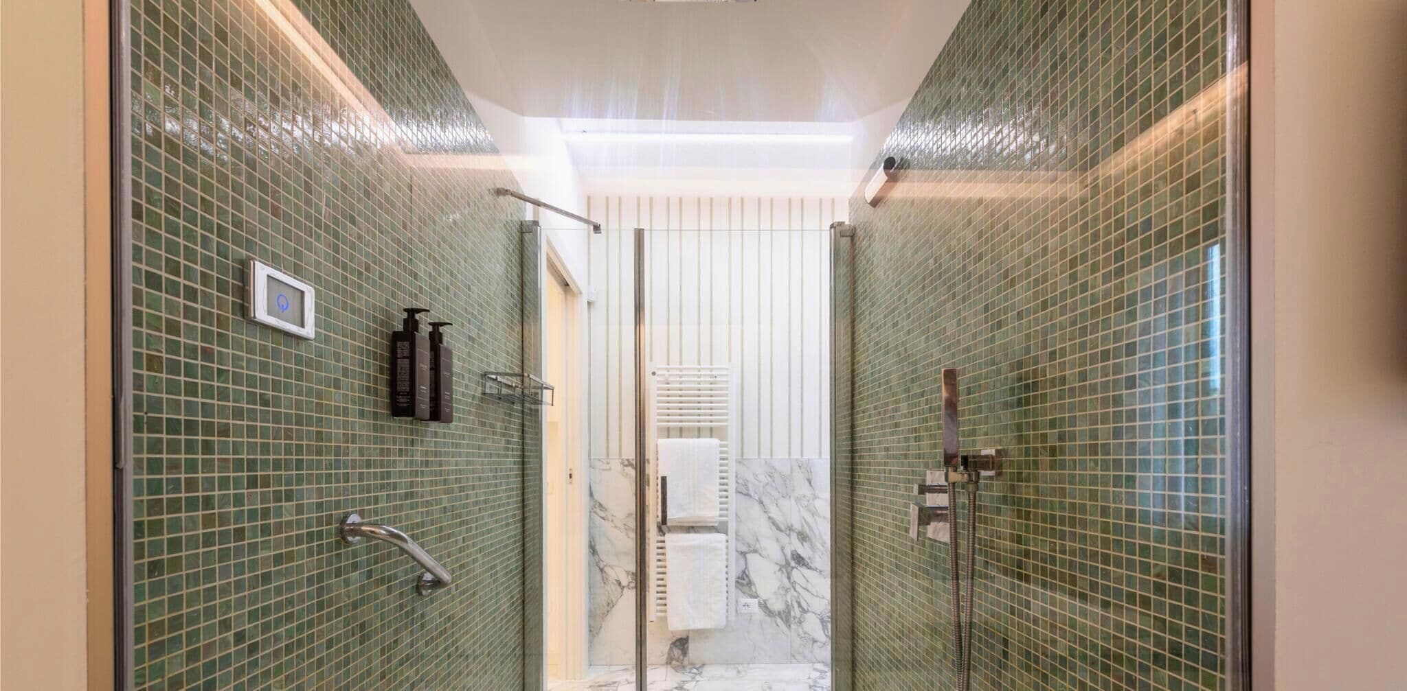 A modern bathroom with green mosaic tiles, a glass shower enclosure, and a marble accent wall.