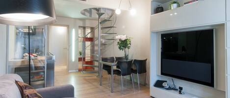 A modern living room with a flat-screen TV, a dining area with a spiral staircase, and a large black lamp.