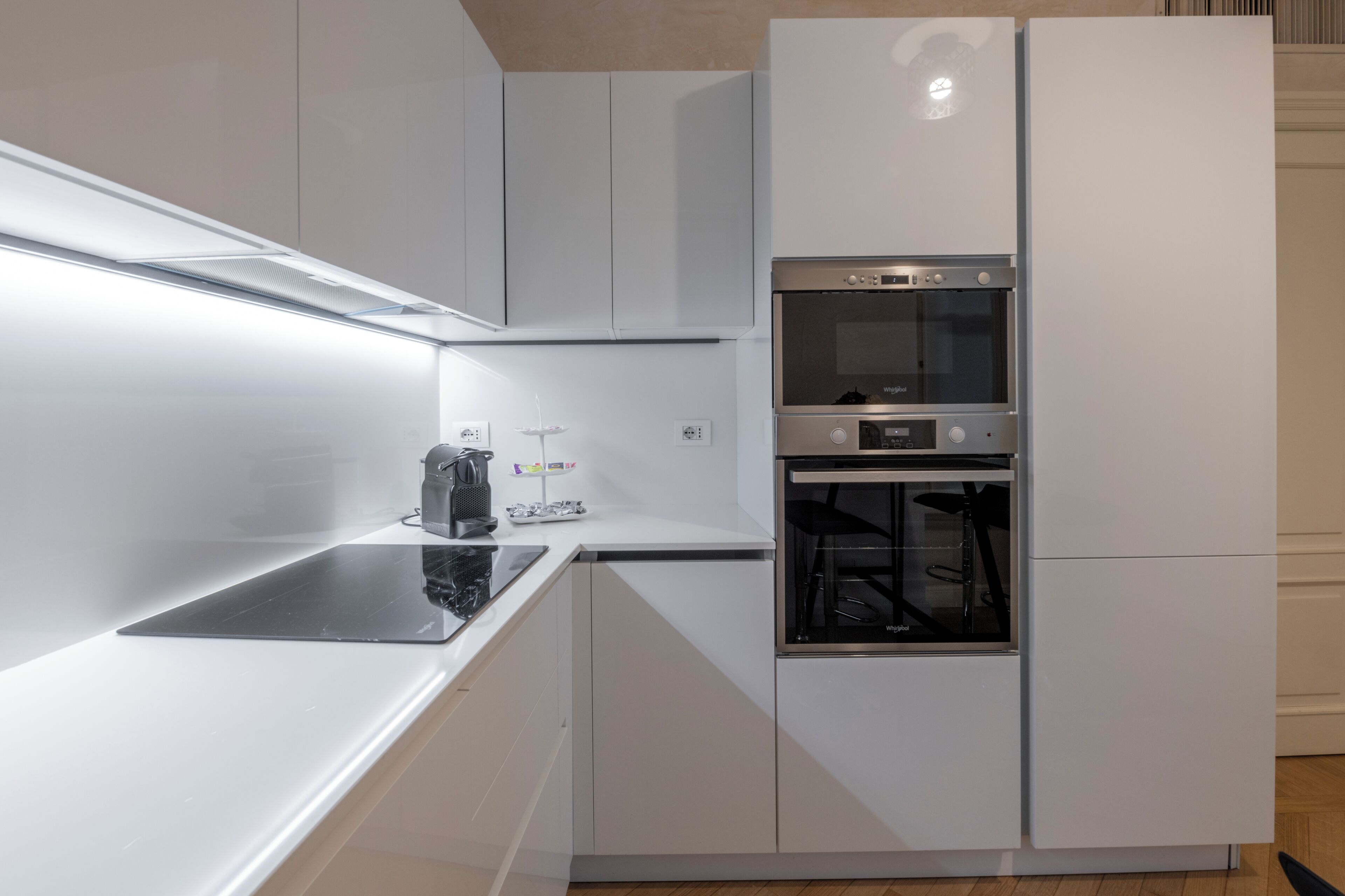 A modern kitchen with white cabinetry, a built-in oven, and a countertop with a kettle.
