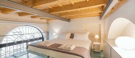 A modern hotel room with a glass floor, a large bed with white linens, a wooden ceiling, and a circular window.