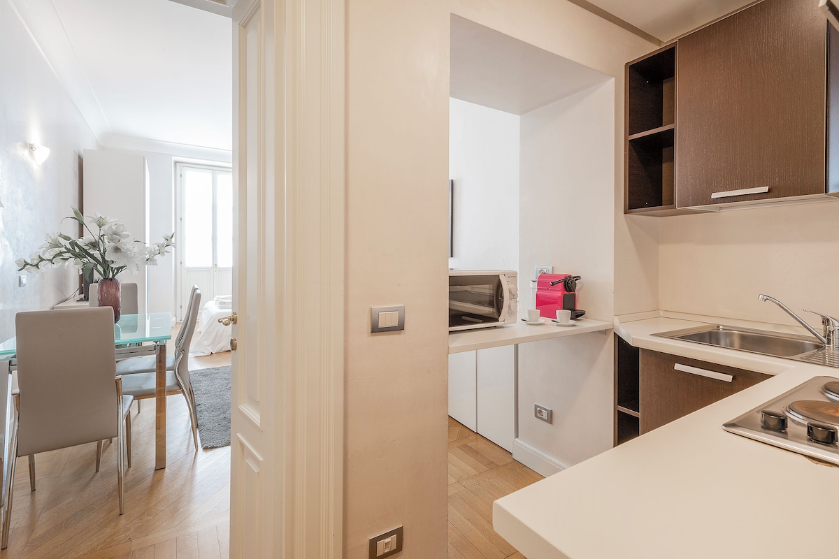 A modern kitchen with white cabinetry, a built-in oven, and a dining area with a glass table and chairs.