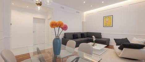 A modern living room with a glass dining table, grey sofas, and a blue vase with flowers.