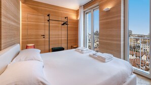 A modern hotel room with a large bed, a wooden wall panel, a view of the city, and a hanging coat rack. - Milan Royal Suites - Brera (Milan)