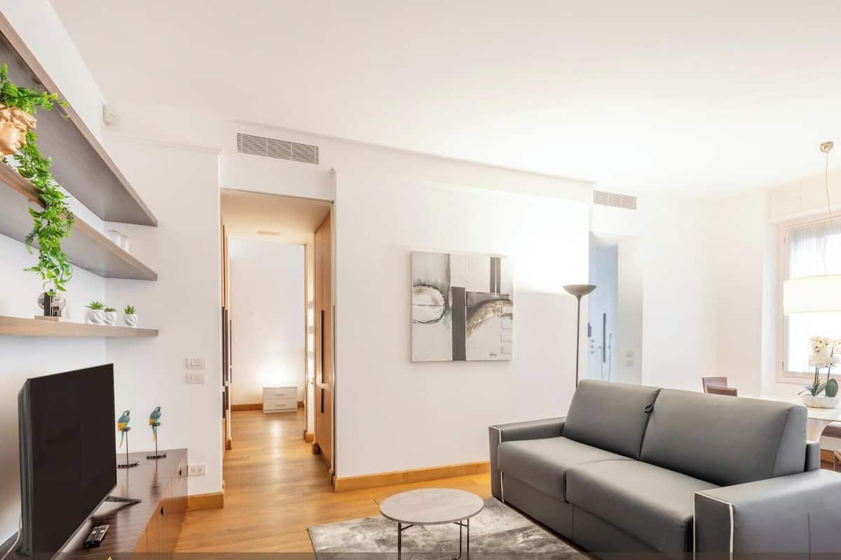 A modern living room with a grey sofa, a flat-screen TV, and a dining area with a table and chairs.