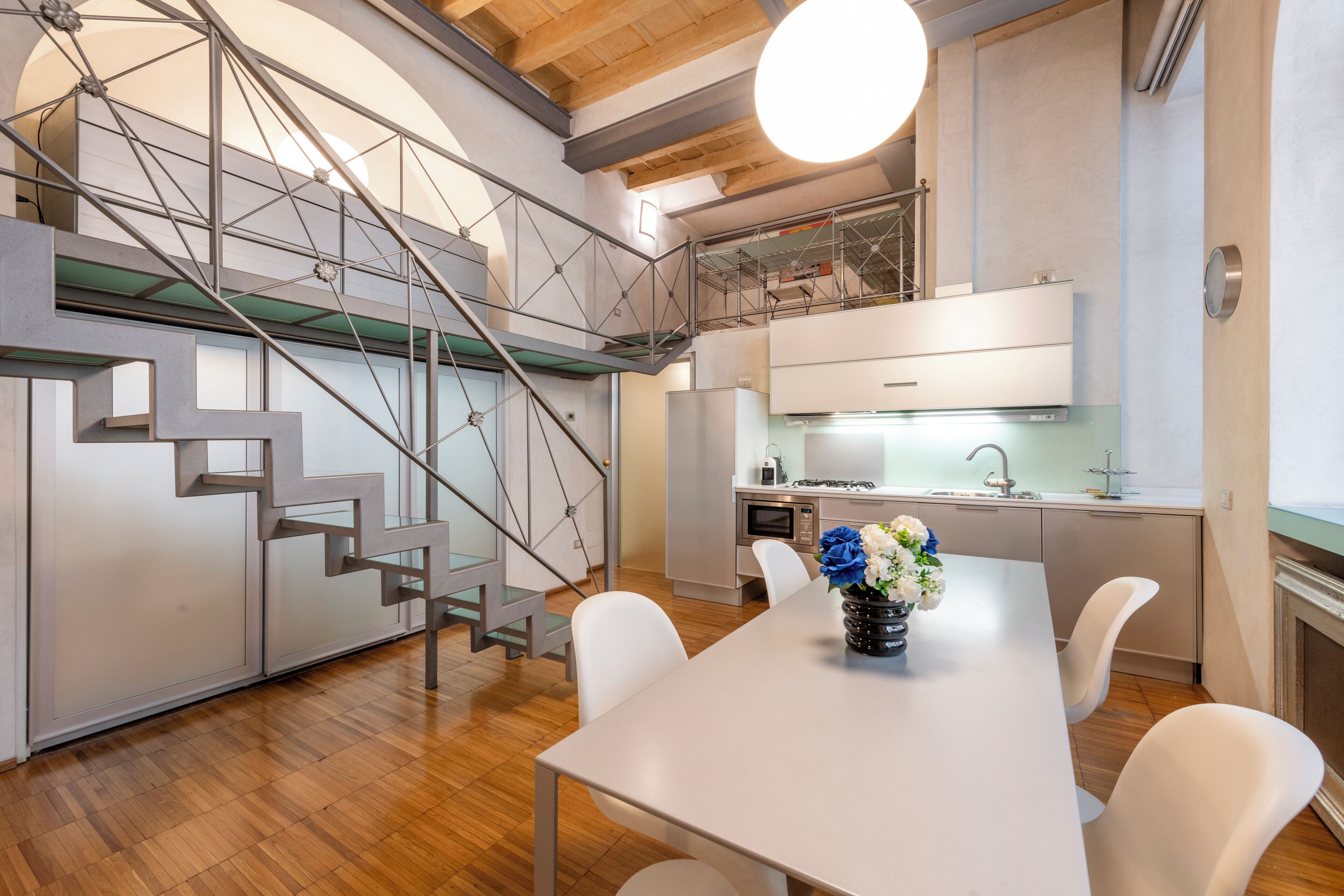 A modern kitchen with white cabinets, stainless steel appliances, and a staircase with glass railings.