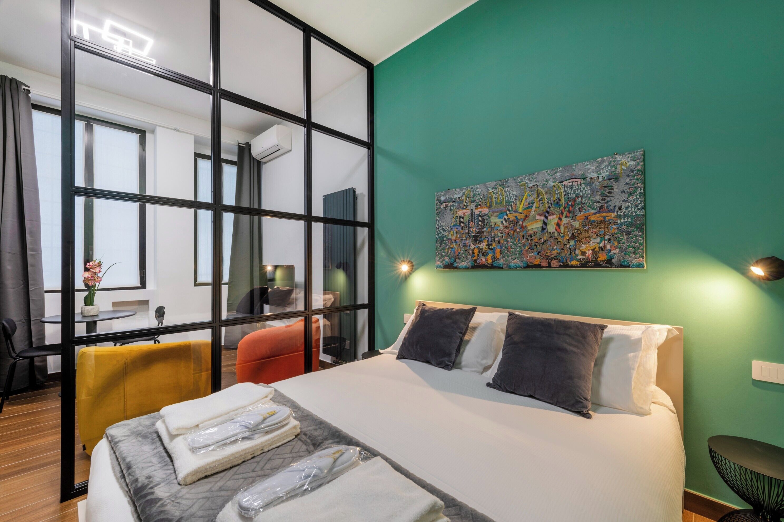 A modern hotel room with a large bed, a green accent wall, and a colorful abstract painting.