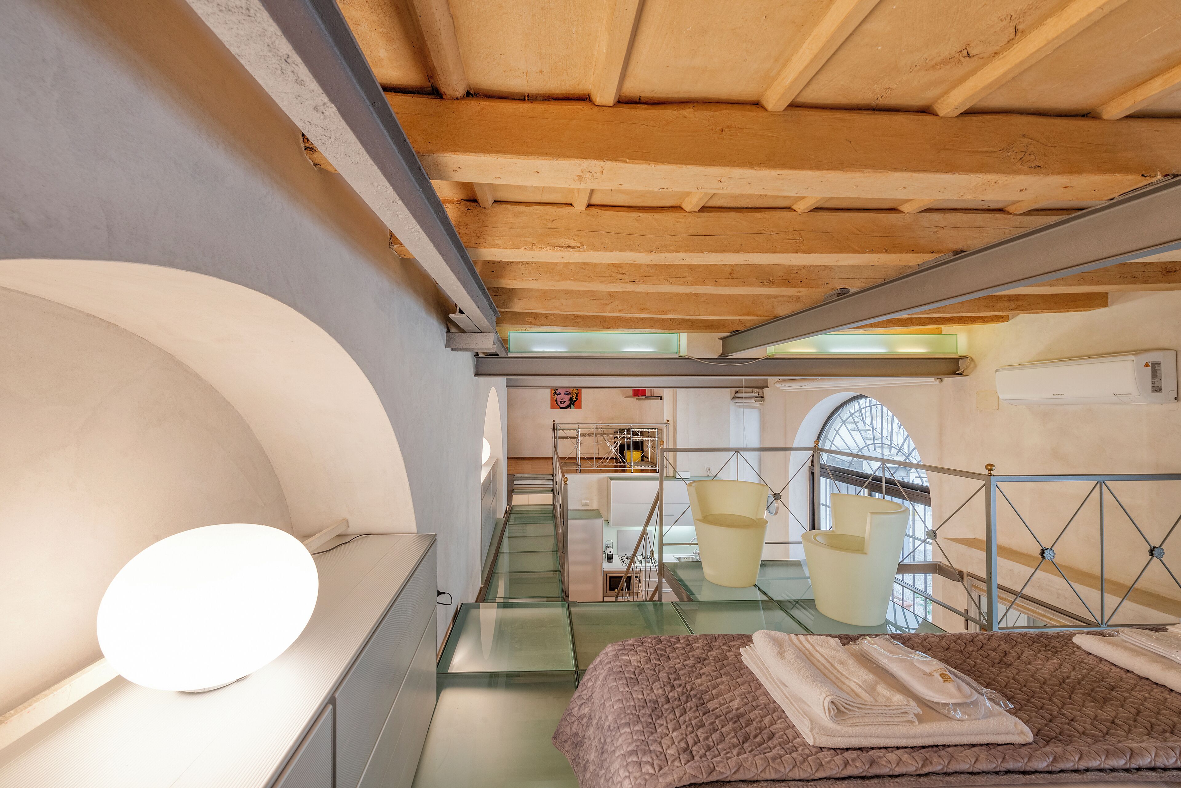 Ein modernes Hotelzimmer mit Glasdecke, einem Bett mit brauner Tagesdecke, einem Nachttisch und einem großen Spiegel.
