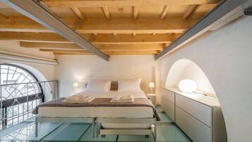 A modern bedroom with a glass floor, a bed with white linens, a round mirror, and a nightstand with a lamp.