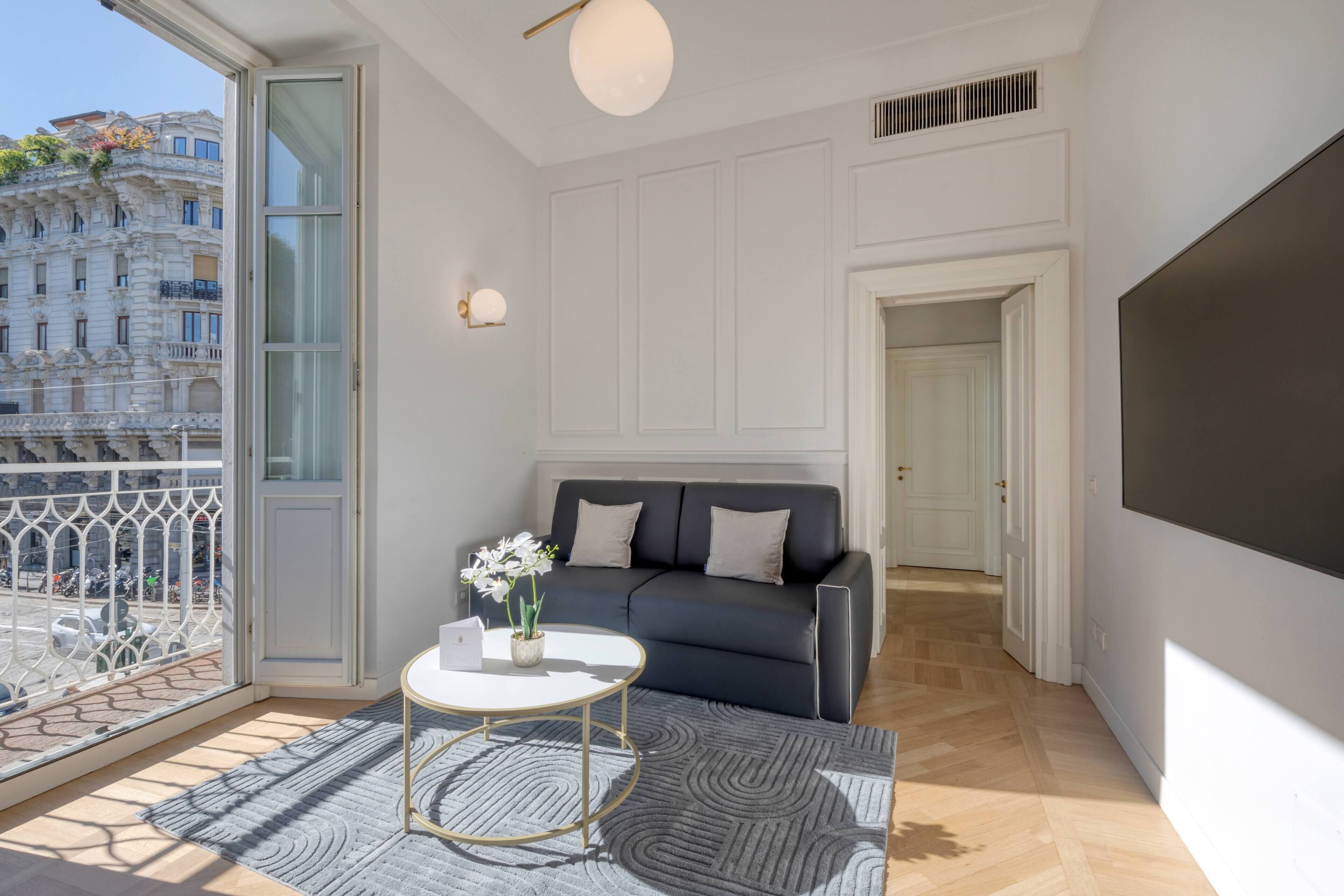 Uma sala de estar moderna com um sofá, uma mesa de centro e vista para o horizonte urbano através de grandes janelas.