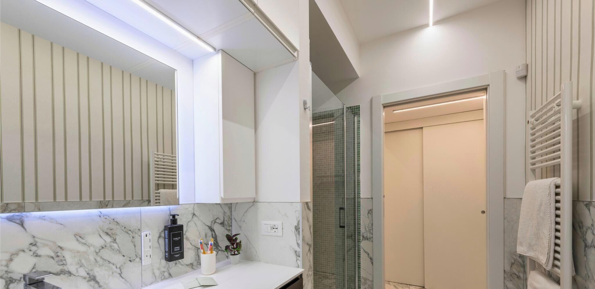 A modern bathroom with a marble countertop, a large mirror, a glass shower enclosure, and a towel rack.