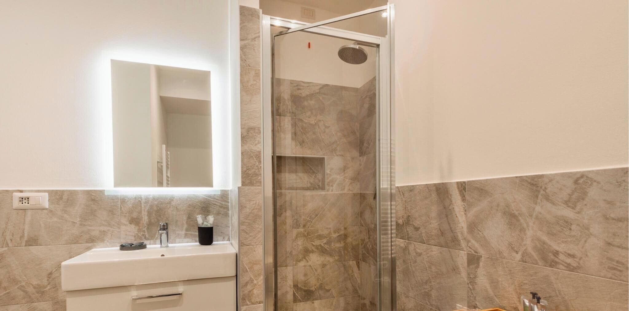 A modern bathroom with a glass-enclosed shower, a white sink with a mirror above it, and marble walls.