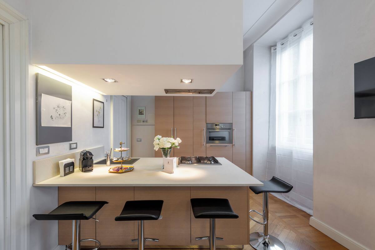 A modern kitchen with a central island, bar stools, and a built-in oven.