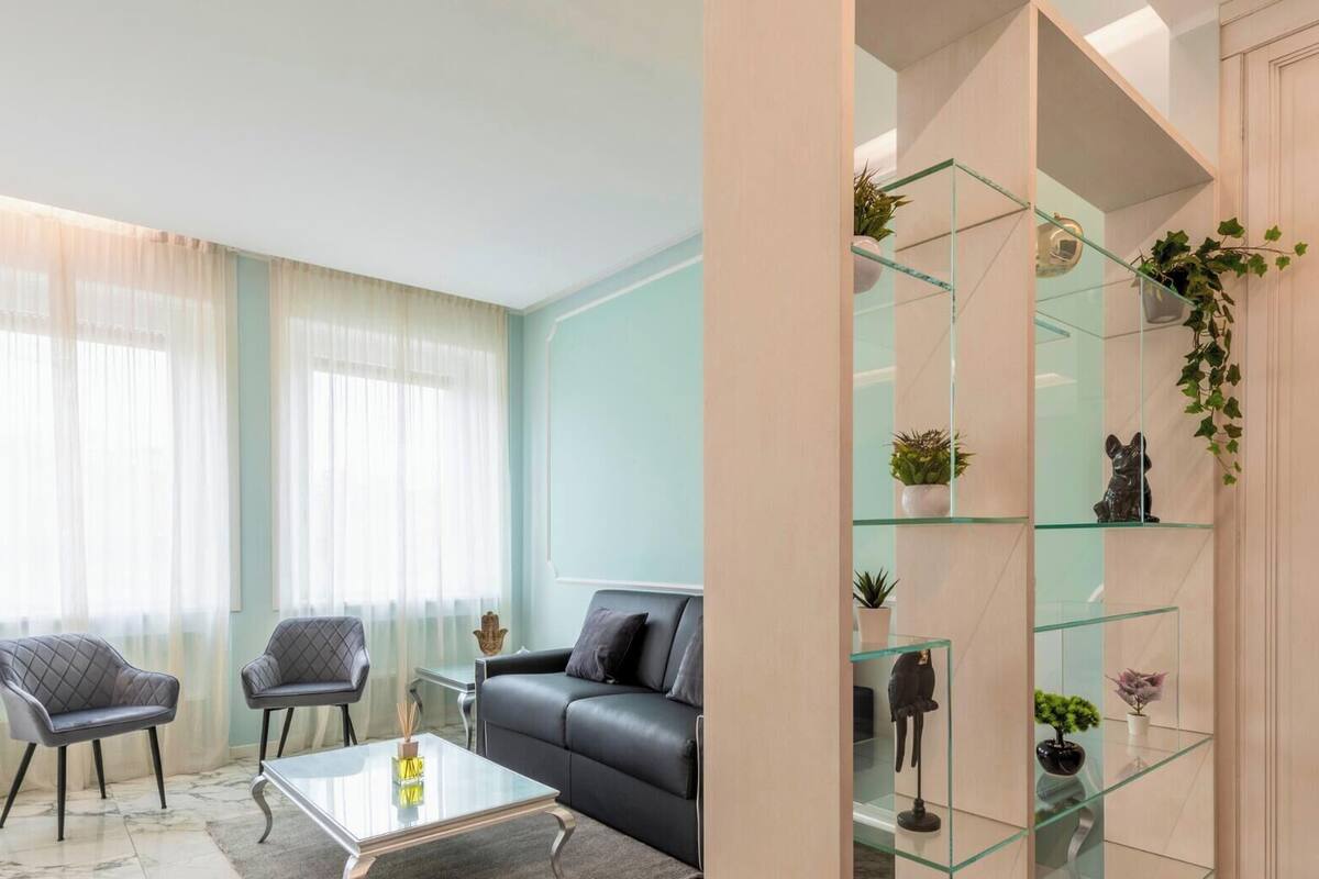 A modern living room with a glass coffee table, two armchairs, a sofa, and a glass shelving unit with plants and decorative items.