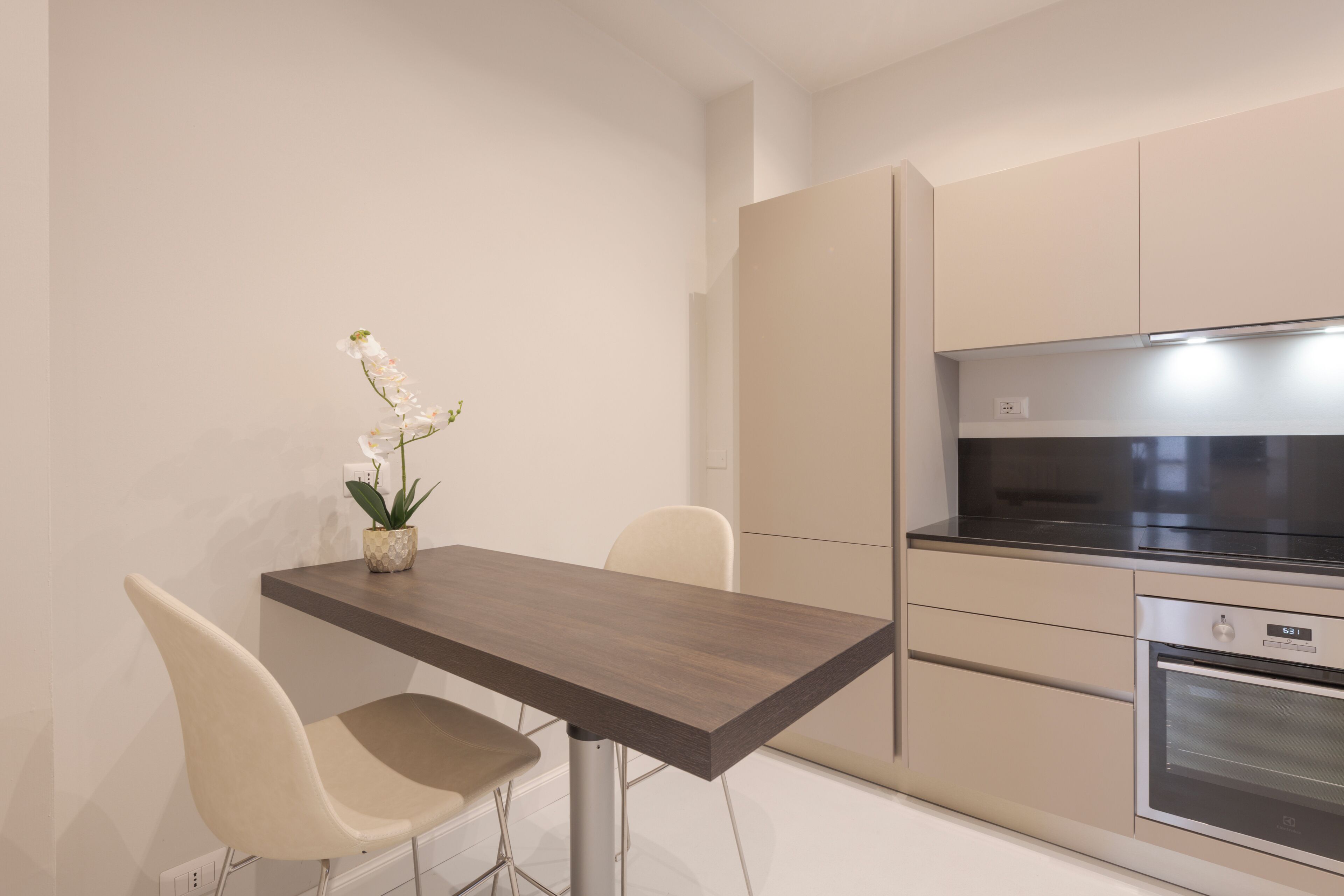 A modern kitchen with a dark wooden table, two white chairs, and a potted orchid.