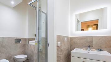 Un baño moderno con cabina de ducha de vidrio, un inodoro, un lavabo con espejo y tocador.