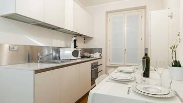Una cucina moderna con mobili bianchi, elettrodomestici in acciaio inossidabile e un'area pranzo per quattro persone.