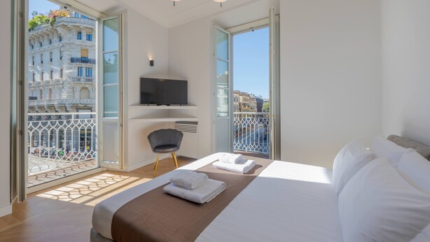 A modern hotel room with a large bed, a flat-screen TV, a balcony with a view of the city, and a chair. - Milan Royal Suites - Brera (Milan)