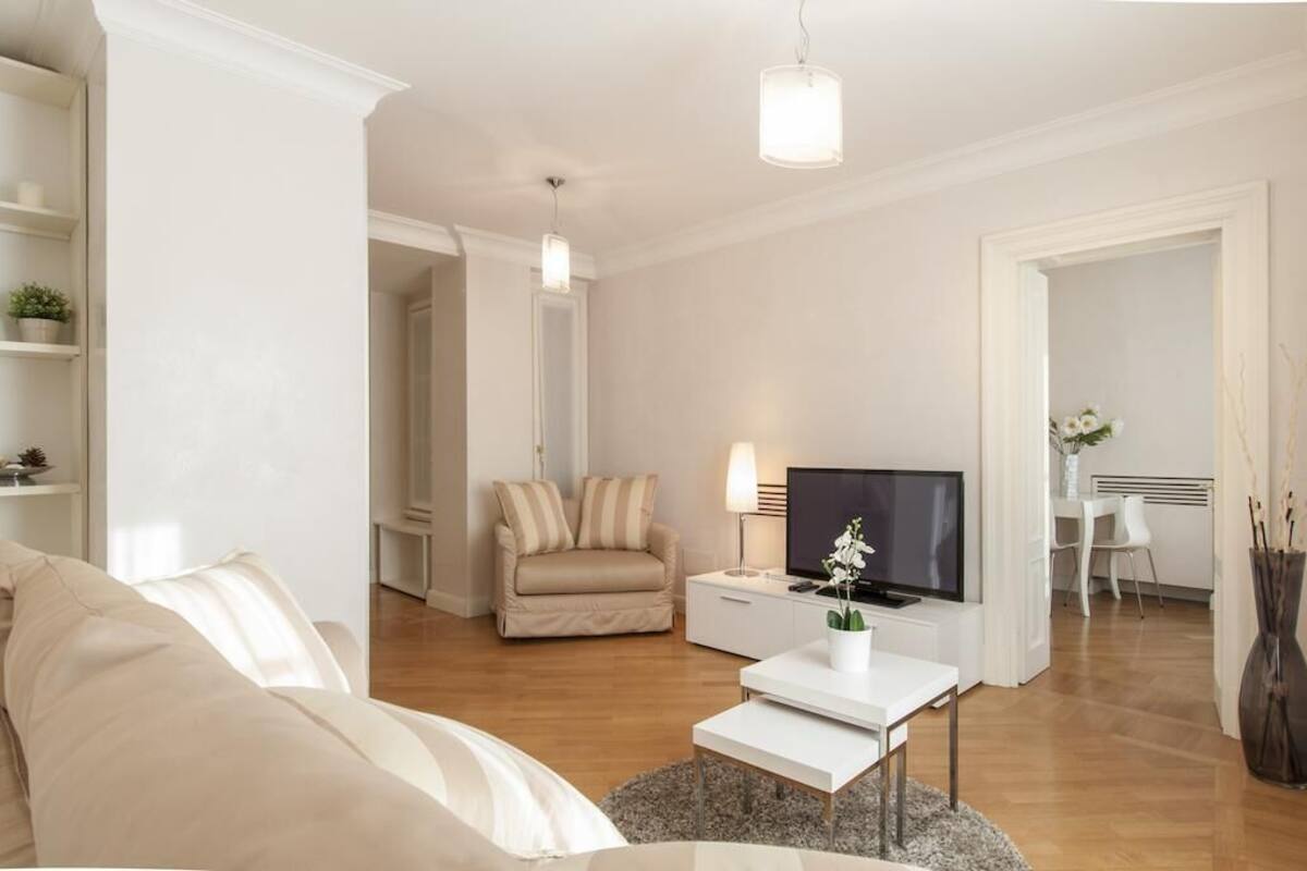A modern living room with a sofa, a coffee table, a TV, and a dining area with chairs.