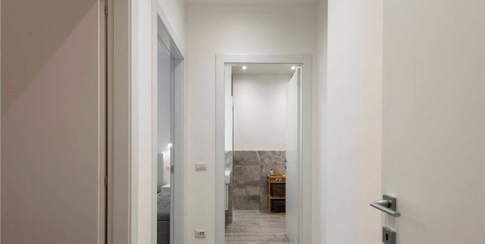 A modern hallway leading to a bathroom with a marble wall and a wooden cabinet.