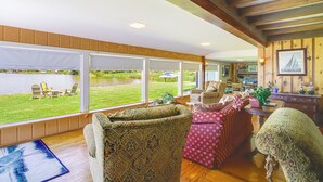 Amplio salón con grandes ventanales con vistas a un lago, amueblado con sofás estampados y suelo de madera.