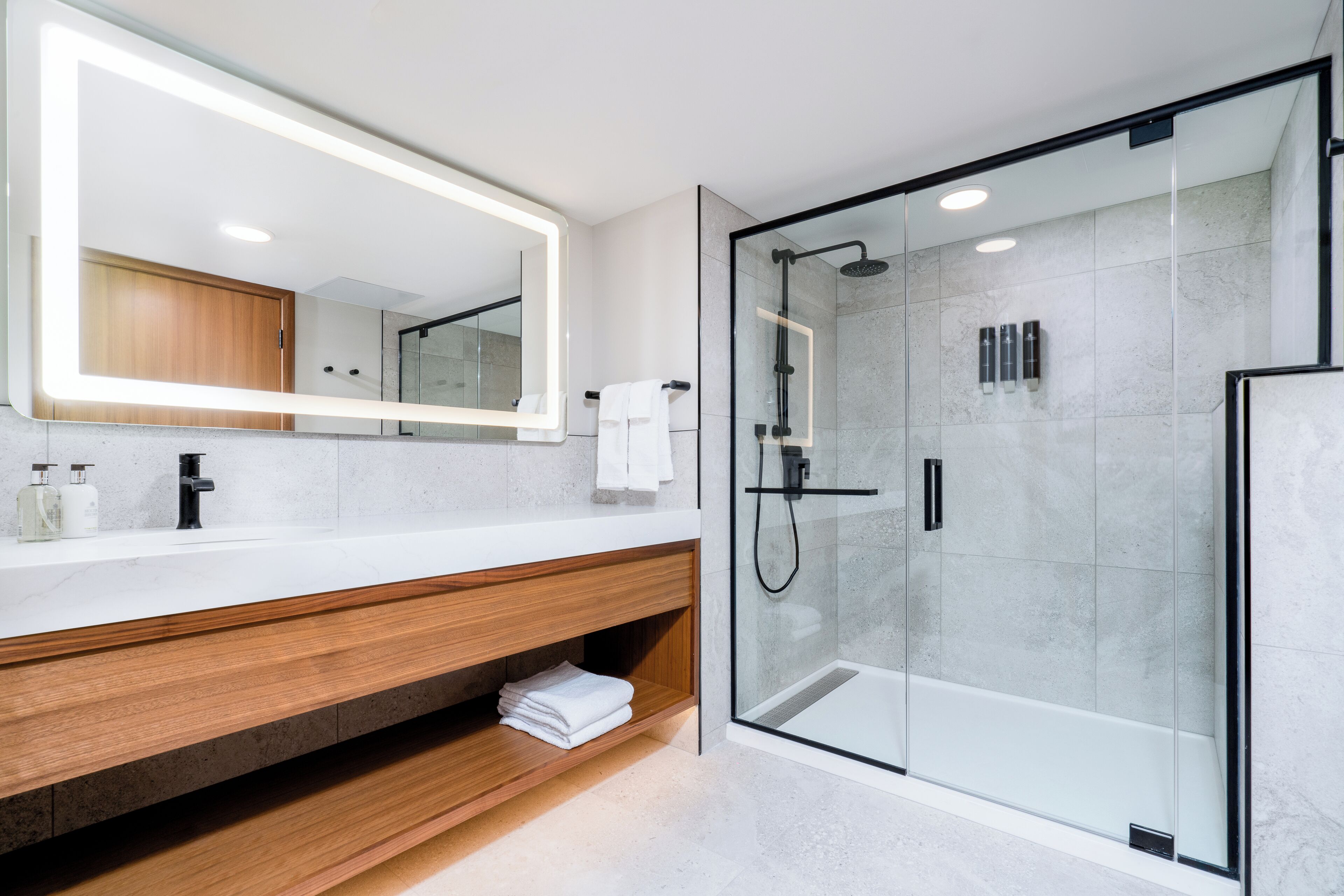 Une salle de bain moderne avec une douche à parois de verre, un grand miroir et un meuble-lavabo en bois.