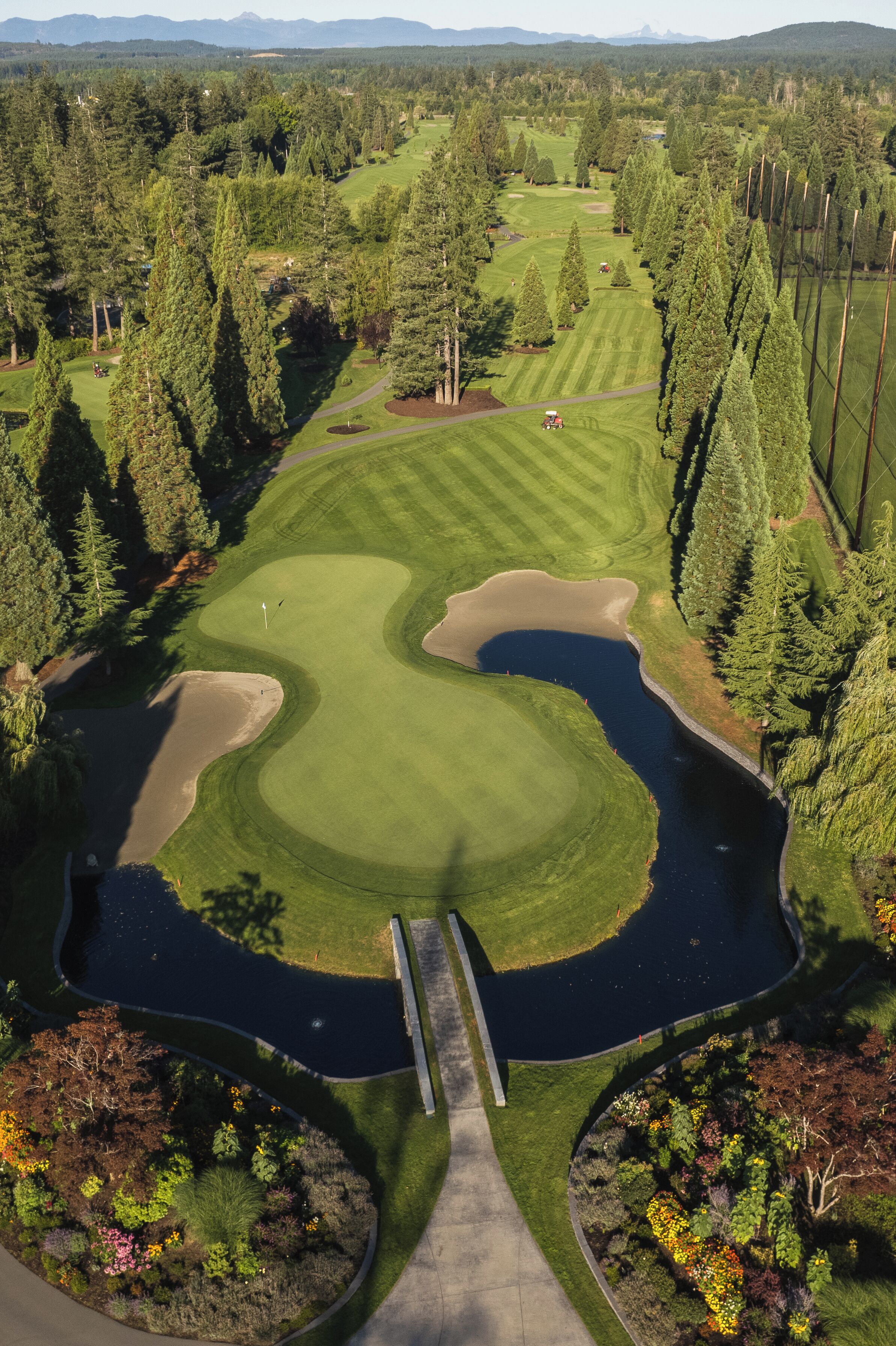 Vista aérea de un campo de golf con un estanque, rodeado de un bosque denso y un puente.