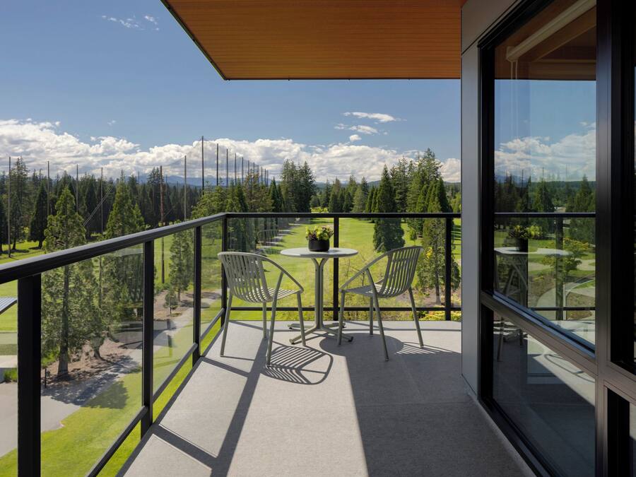 Een balkon met een tafel en stoelen met uitzicht op een bebost gebied.
