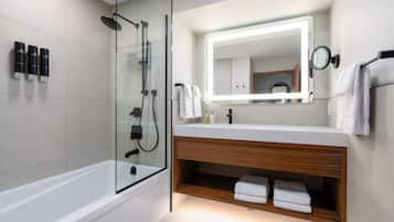 Un baño moderno con ducha envuelta en vidrio, tocador con espejo y toallas ordenadas.
