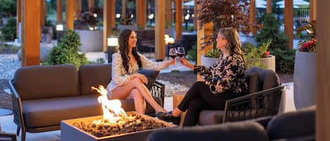 An outdoor seating area with a fire feature, wooden pergola, and potted plants.