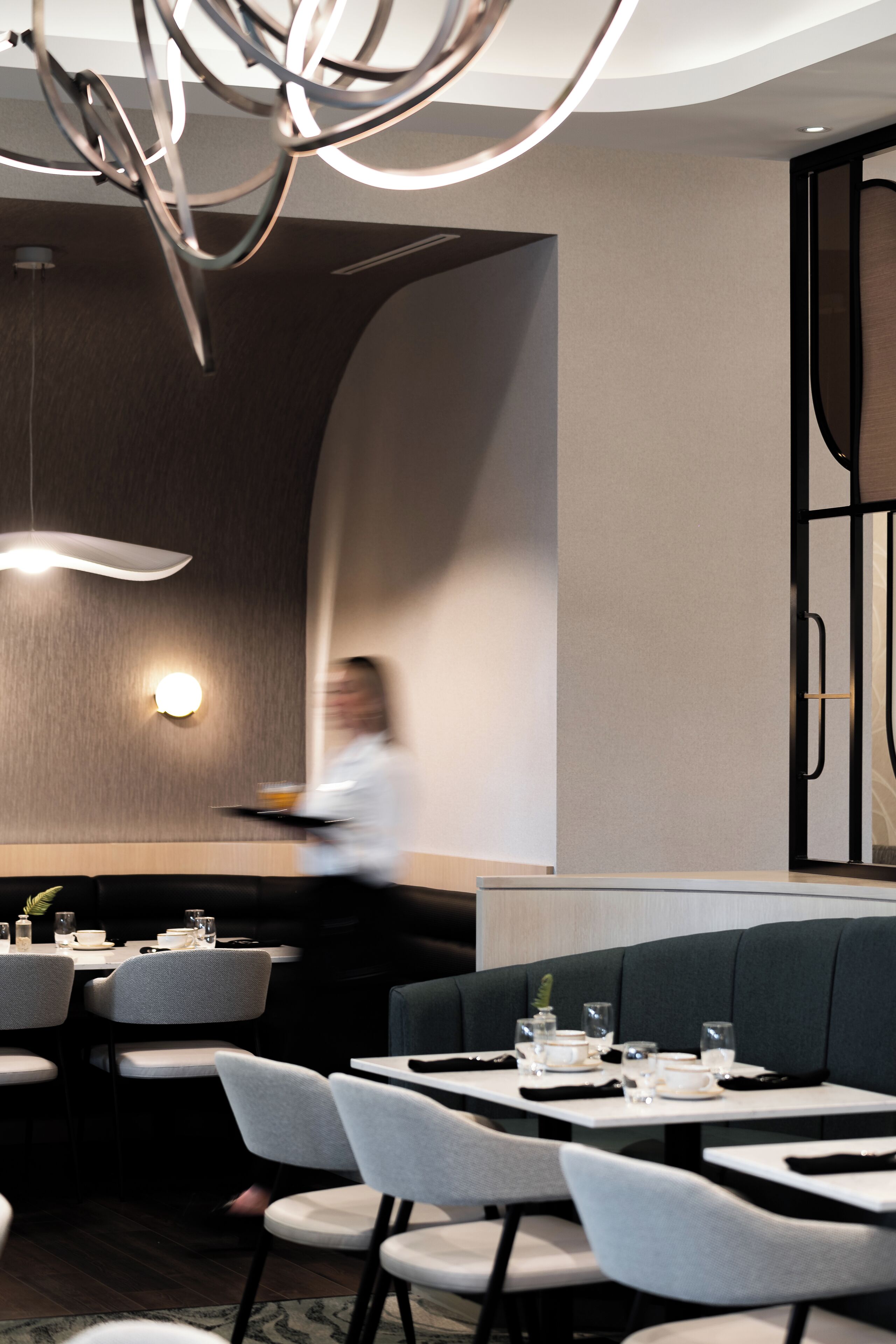Un interior de restaurante moderno con mesas redondas, asientos tapizados en gris y lámparas contemporáneas.
