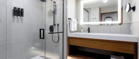 Un baño moderno con cabina de ducha acristalada, tocador con encimera de madera y un espejo grande con iluminación integrada.