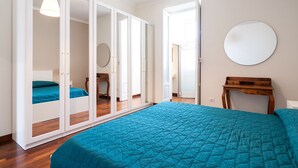 Une chambre avec un grand lit, une armoire aux portes miroir, un grand miroir rond accroché au mur et une petite table en bois.